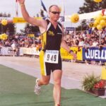 Ein Läufer mit erhobenen Arm im Zieleinlauf des Ironman Roth auf grünem Untergrund ist zu sehen