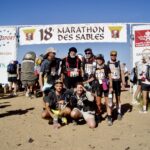 Zieleinlauf des MDS in der Sahara. Unter dem Banner ist eine Gruppe in Laufkleidung zu sehen
