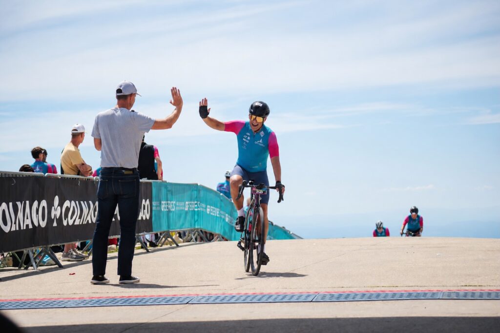 Man sieht einen Rennradfahrer der kurz vor einem Handshake auf dem Gipfel des Mont Ventoux bei bestem Wetter ist